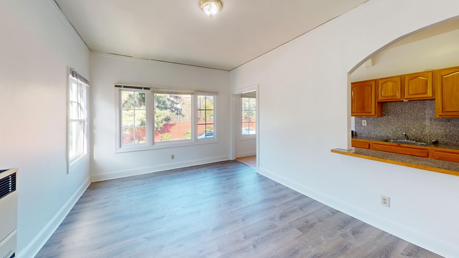 A spacious room with wooden floors and a window overlooking a garden.